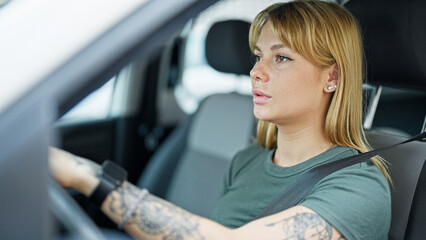 Young blonde woman driving car with relaxed expression at street