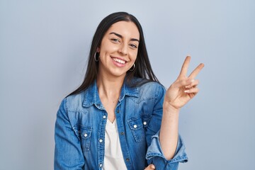 Hispanic woman standing over blue background smiling with happy face winking at the camera doing...