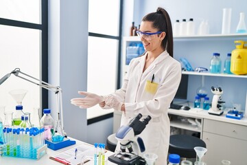 Young beautiful hispanic woman scientist smiling confident wearing gloves at laboratory