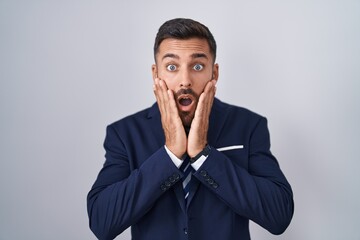 Handsome hispanic man wearing suit and tie afraid and shocked, surprise and amazed expression with...