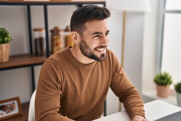 Naklejka premium Young hispanic man smiling confident sitting on table at home