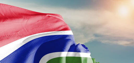 The Gambia national flag cloth fabric waving on beautiful sky Background.