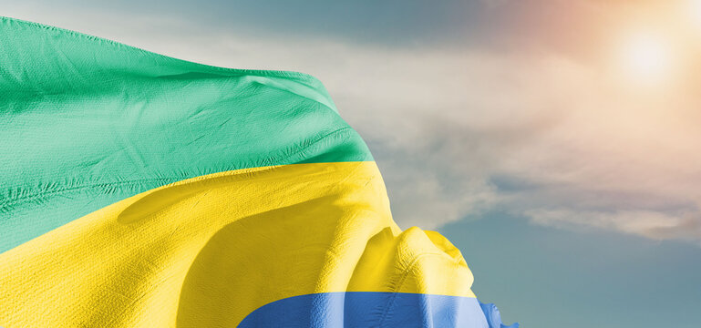 Gabon national flag cloth fabric waving on beautiful sky Background.