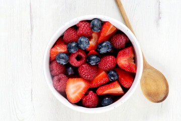 White bowl with red fruits on white wooden board
