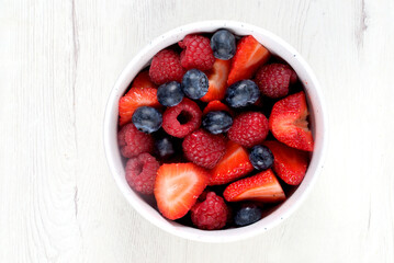 White bowl with red fruits on white wooden board