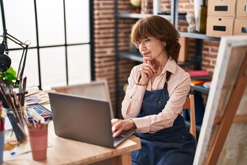 Middle age woman artist using laptop with doubt expression at art studio