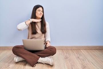 Young brunette woman working using computer laptop sitting on the floor cutting throat with hand as knife, threaten aggression with furious violence