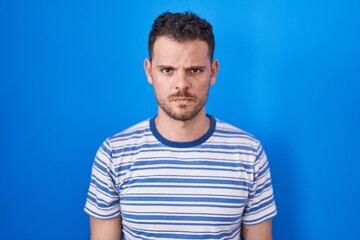 Fototapeta premium Young hispanic man standing over blue background skeptic and nervous, frowning upset because of problem. negative person.