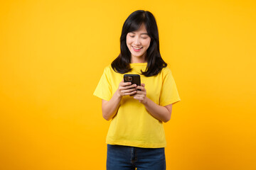 Experience the happiness and connection of technology with joyful portrait. young Asian woman wearing yellow t-shirt and denim jeans smiles using smartphone. concept of technology and smartphone app.
