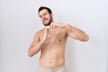 Fototapeta premium Young hispanic man standing shirtless over white background smiling in love doing heart symbol shape with hands. romantic concept.