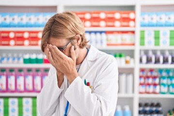 Caucasian man with mustache working at pharmacy drugstore with sad expression covering face with...
