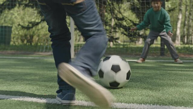 Ground level slow mo shot of kid running on soccer field and shooting ball while playing with friend outdoors on summer day