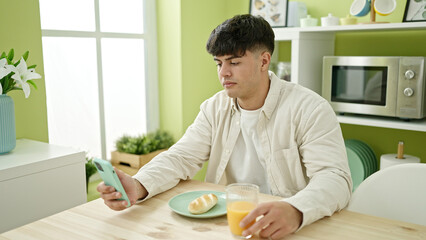 Fototapeta na wymiar Young hispanic man using smartphone having breakfast at dinning room