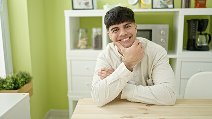 Obraz premium Young hispanic man sitting on table smiling confident at dinning room