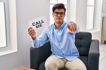 Hispanic man working at therapy office holding call me banner pointing with finger to the camera...