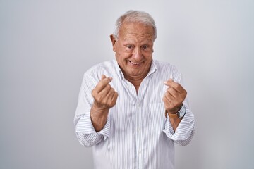 Senior man with grey hair standing over isolated background doing money gesture with hands, asking for salary payment, millionaire business