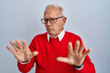 Senior man with grey hair standing over isolated background moving away hands palms showing refusal...