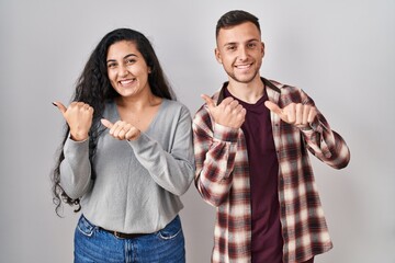 Young hispanic couple standing over white background pointing to the back behind with hand and...