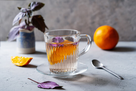 Healthy and immune boosty purple basil tea in a glass mug with slices of orange and fresh basil backside. Grey concrete background