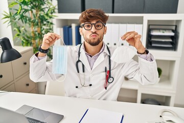 Arab man with beard wearing doctor uniform holding medical mask looking at the camera blowing a kiss being lovely and sexy. love expression.