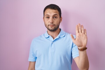Hispanic man standing over pink background doing stop sing with palm of the hand. warning expression with negative and serious gesture on the face.