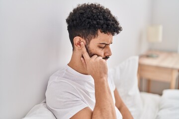 Young arab man suffering for ear pain sitting on bed at bedroom - obrazy, fototapety, plakaty