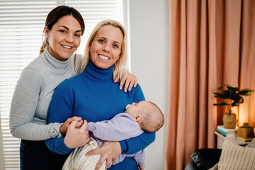 Fototapeta premium Gay lesbian couple and newborn baby having tender moment indoors at home - Lgbt family concept - Focus on infant head
