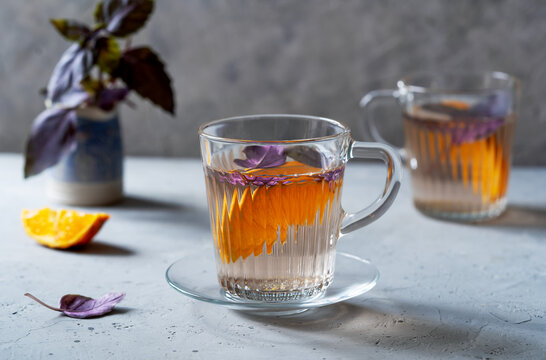 Healthy and immune boosty purple basil tea in a glass mugs with slices of orange and fresh basil backside. Grey concrete background