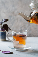 Healthy purple basil tea in a glass mug with slice of orange, tea is pouring from teapot, fresh...