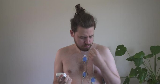 Young man looking concerned about heart monitor, heart monitor or ECG/EKG attached to check heart health in hospital or medical clinic. Using AI assisted medical technology. Troubleshooting equipment.