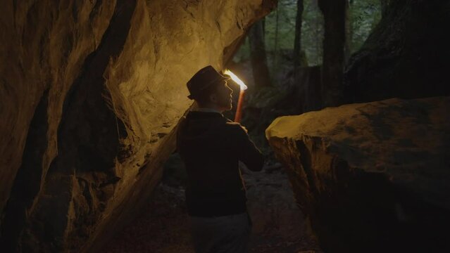 Young Man Discovering Stone Cave Outdoors at Night Holding Torchlight
