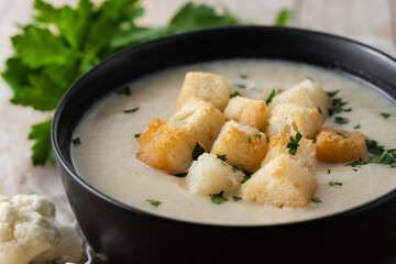 Cauliflower soup in a bowl on wooden table. Close up
