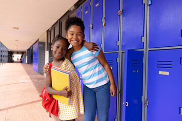 Portrait of happy african american schoolchildren standing next to locker at school