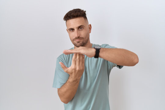 Hispanic man with beard standing over white background doing time out gesture with hands, frustrated and serious face