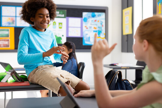 Happy diverse schoolchildren using sign language in school classroom