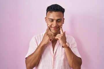 Fototapeta na wymiar Young hispanic man standing over pink background smiling with open mouth, fingers pointing and forcing cheerful smile
