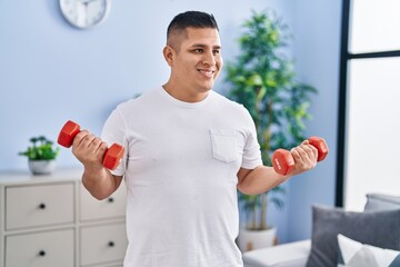 Young latin man smiling confident using dumbbells training at home