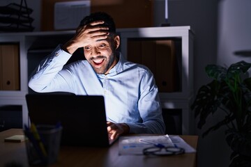 Hispanic man with beard working at the office with laptop at night stressed and frustrated with hand on head, surprised and angry face
