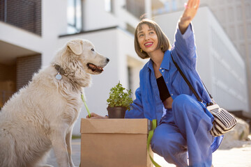 Woman cares her dog while sitting with cardboard box and flowerpot, relocating to a new house....
