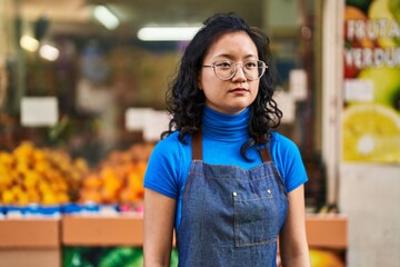 Young chinese woman employee standing with serious expression at fruit store