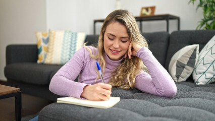 Young blonde woman writing on notebook sitting on floor at home