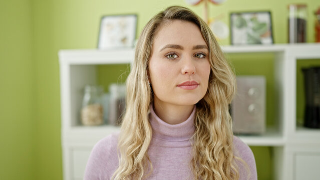 Young blonde woman sitting on table with serious expression at dinning room