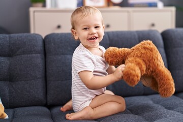 Adorable toddler playing with teddy bear sitting on sofa at home