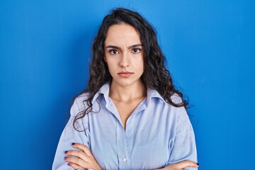Obraz premium Young brunette woman standing over blue background skeptic and nervous, disapproving expression on face with crossed arms. negative person.