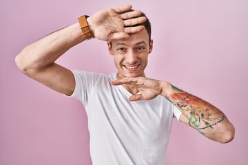 Caucasian man standing over pink background smiling cheerful playing peek a boo with hands showing...