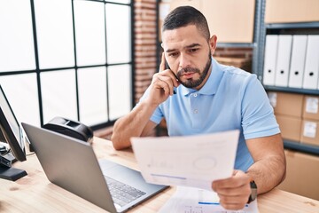 Fototapeta premium Young latin man ecommerce business worker reading document talking on smartphone at office