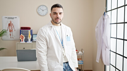 Young hispanic man doctor standing with serious expression at clinic