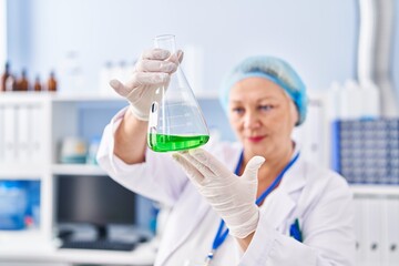 Fototapeta premium Middle age blonde woman wearing scientist uniform holding test tube at laboratory