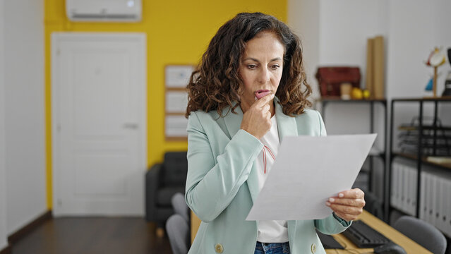 Middle age hispanic woman business worker reading document with doubt expression at office