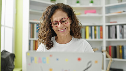 Middle age hispanic woman student using laptop studying at library university